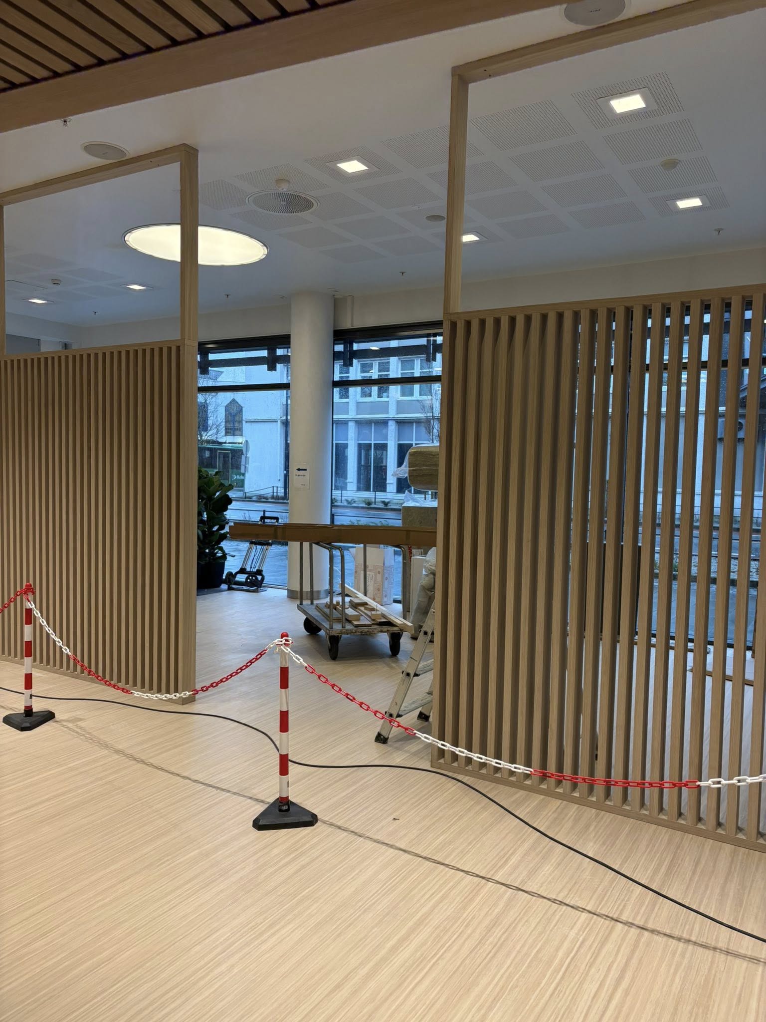Skillevegg med vertikale trespiler og glassdør under montering i et banklokale