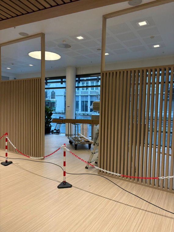 Romdeler med vertikale trespiler og glassfelt under montering, området sperret av med bånd