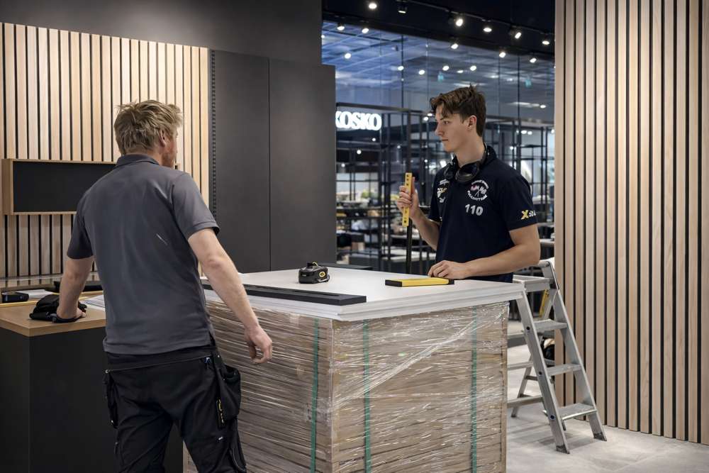 To montører fra Via Montasje setter opp en resepsjonsdisk foran vegg med trespiler